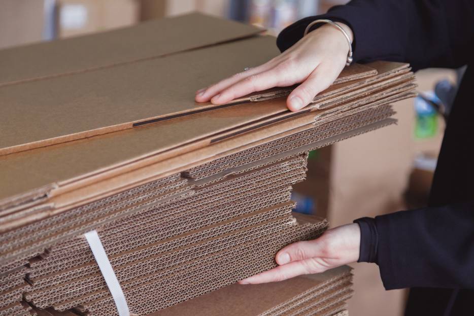 trabajadora toma pliegos de cajas de cartón para empaque manual